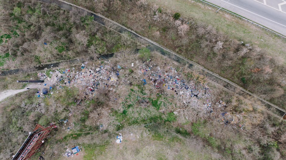 A large pile of black rubbish bags filled with waste are stacked against a tiled urban wall, with some of the bags appearing torn or squeezed. Several discarded plastic water bottles are visible among
